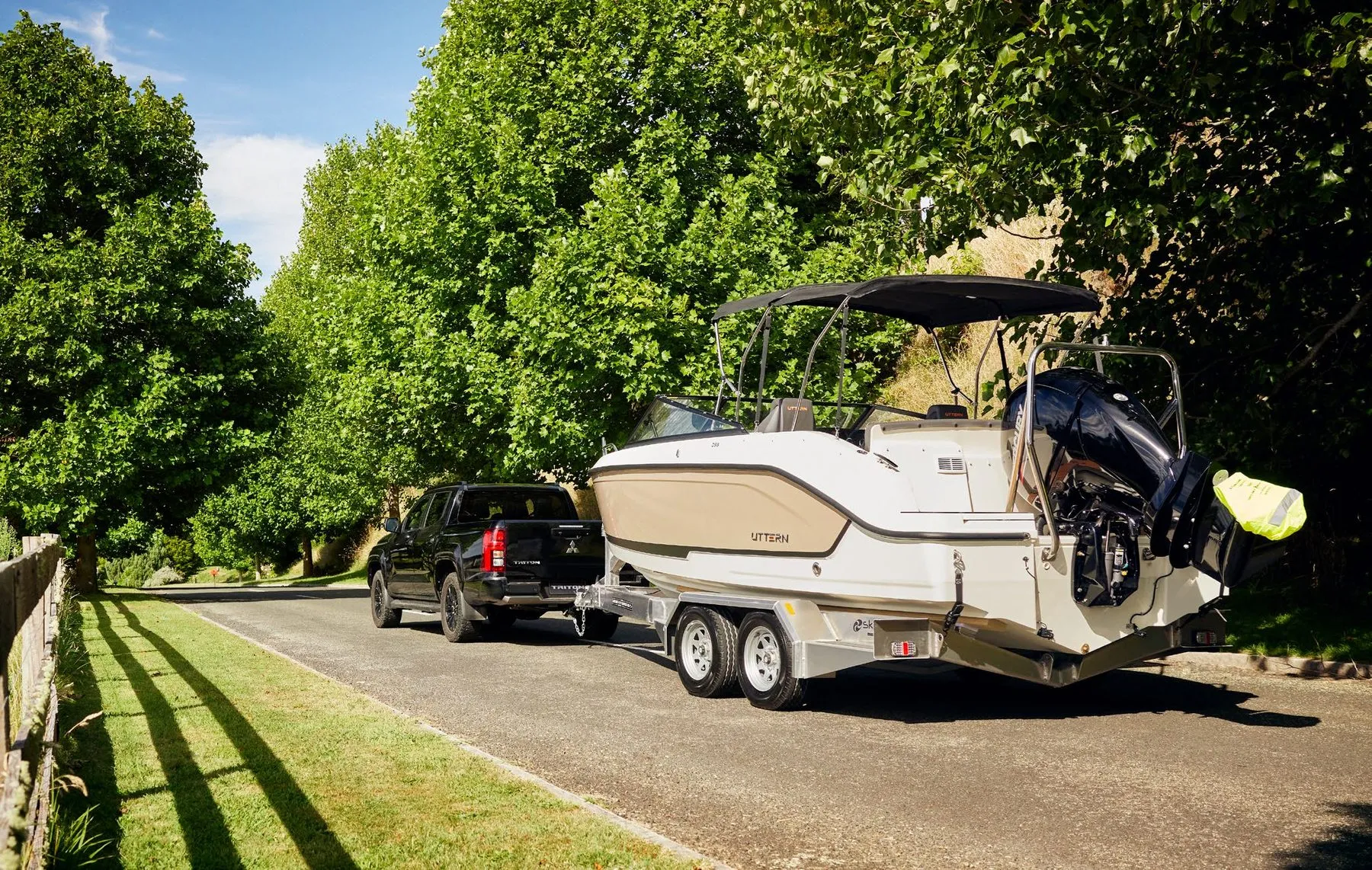 Black Mitsubishi Triton towing a boat on a tree-lined road