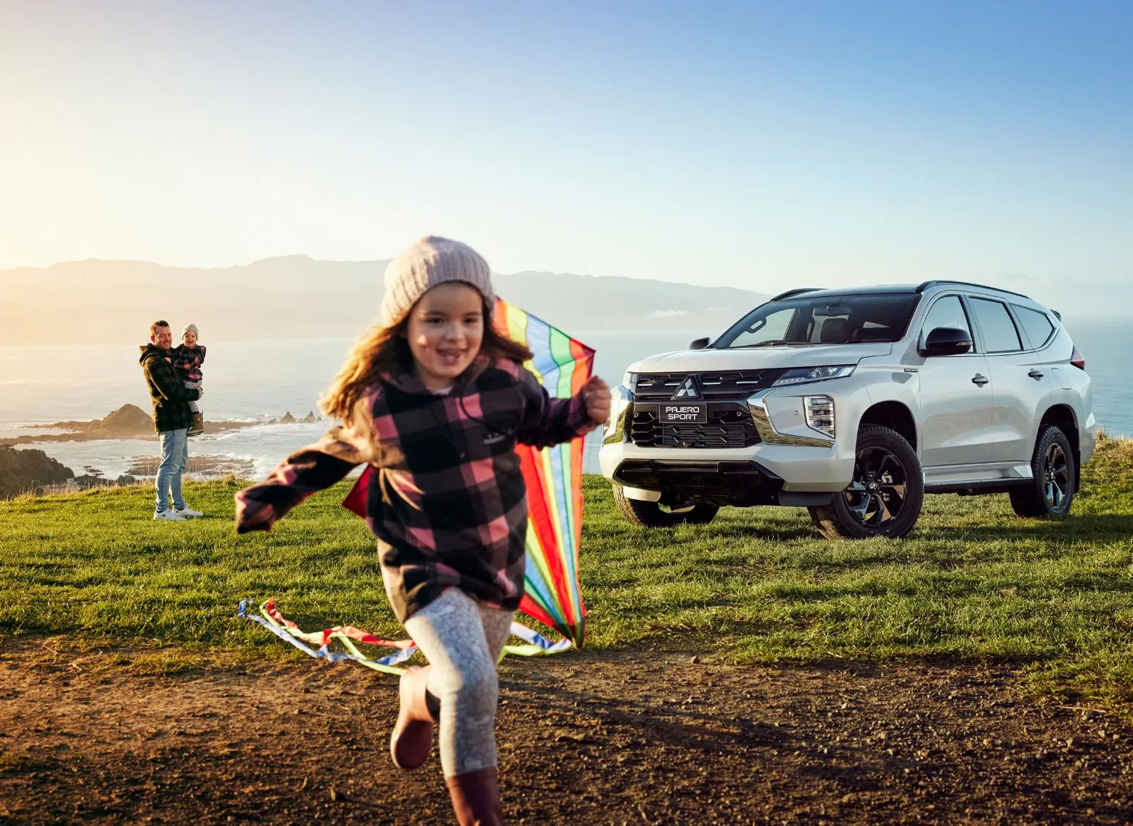 Family flying a kite beside a Mitsubishi Pajero Sport